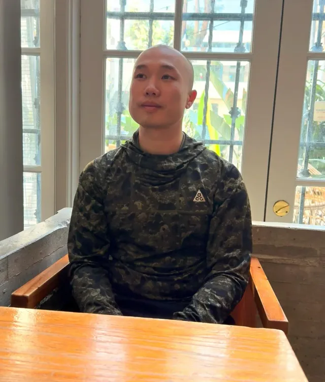 A person in a patterned long-sleeved shirt sitting at a table.