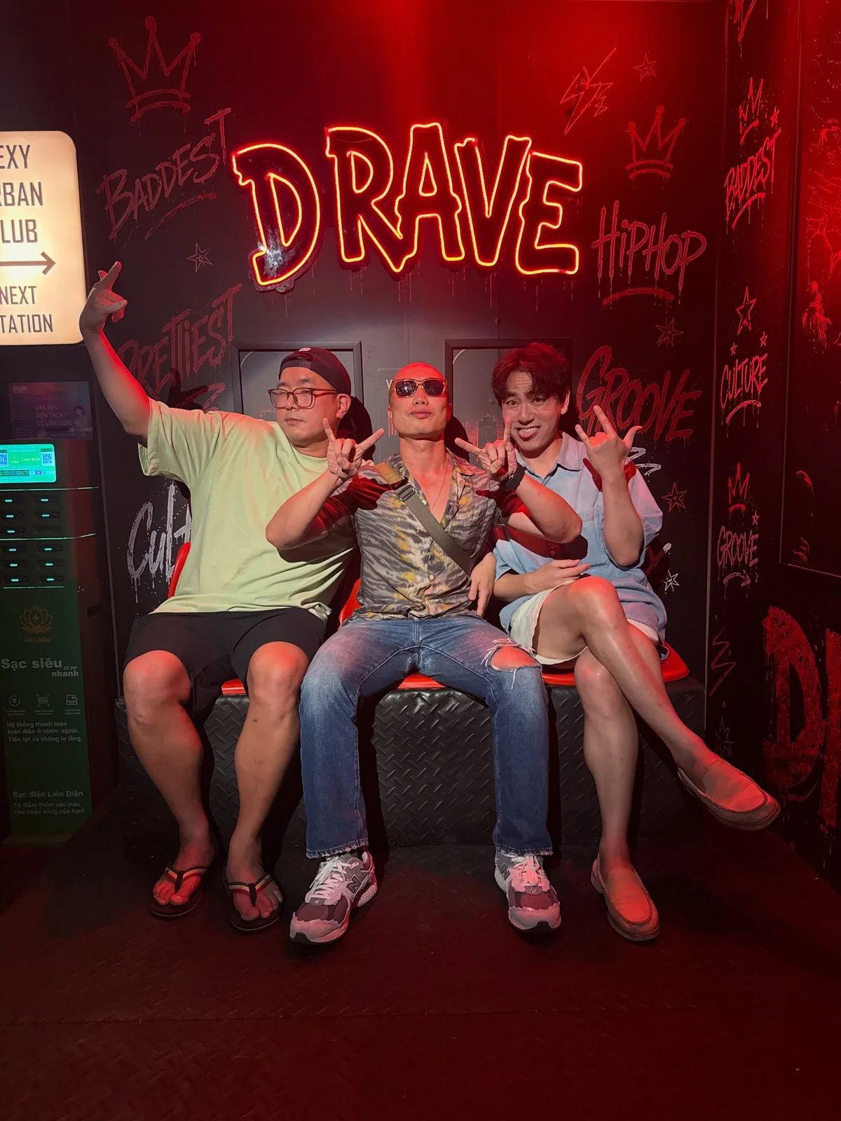 Three people sitting beneath a red neon sign.